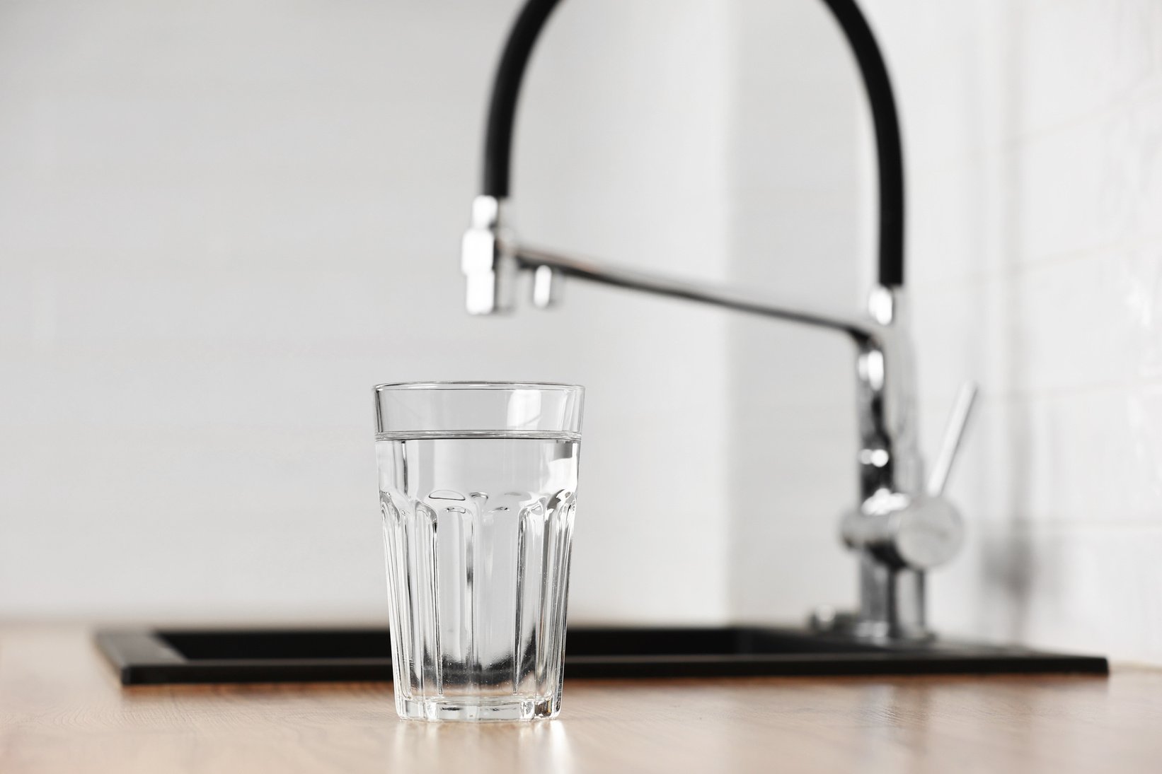 Transparent glass of clean filtering water on wooden table in kitchen interior. Tap with purified water with an osmosis system of the home kitchen sink